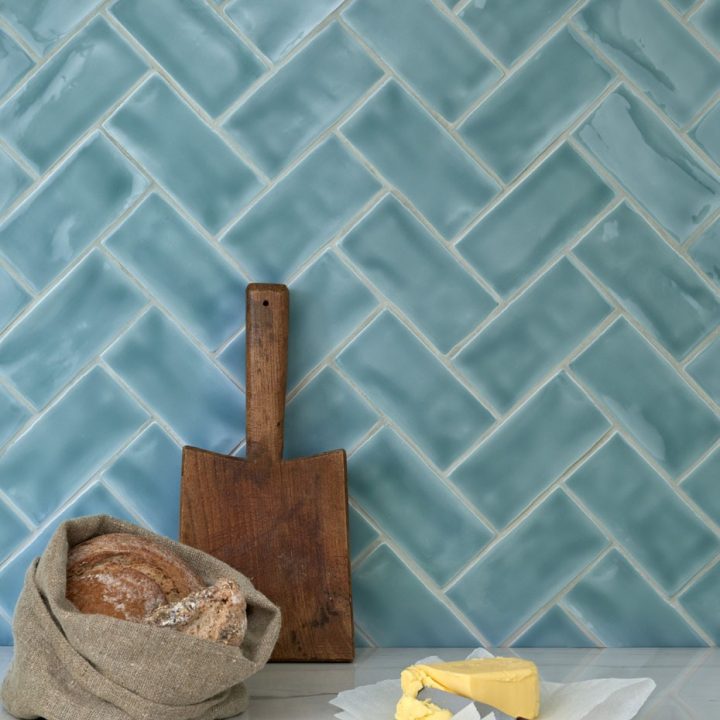 Wall of gloss bright blue green medium metro tile laid in a herringbone tile pattern behind kitchenware
