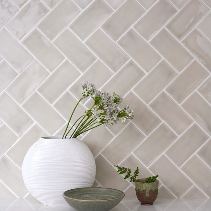 Wall of gloss warm grey medium metro tile laid in a vertical herringbone tile pattern behind home accessories