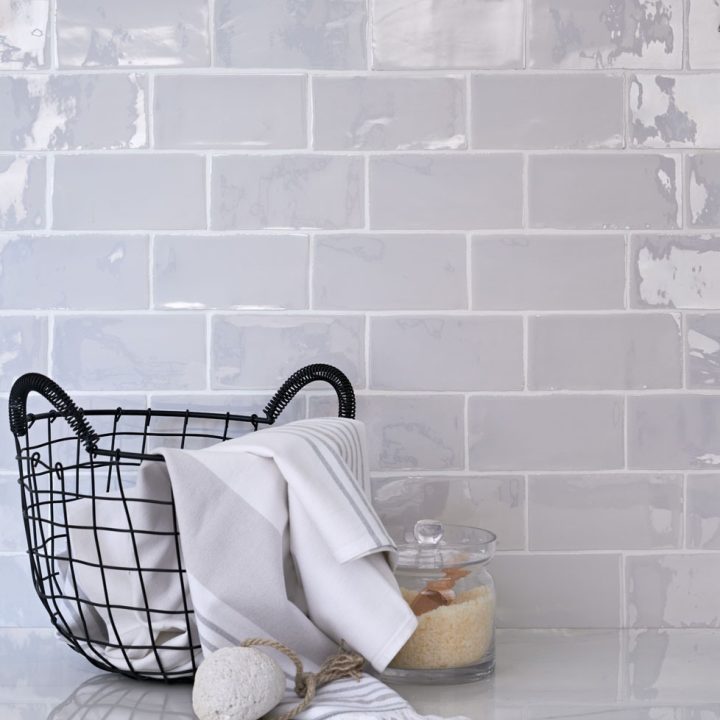 Wall of lustre iridescent white medium metro tile laid in a brick bond tile pattern behind basket and bathroom accessories