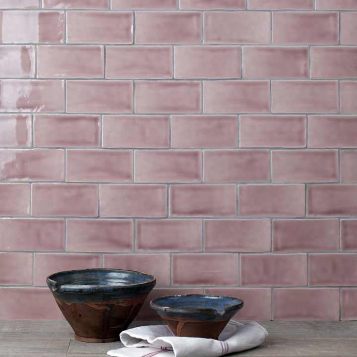 Wall of gloss dusky rose pink medium metro tile laid in a herringbone tile pattern behind home accessories