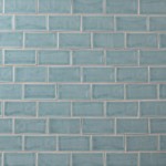 Wall of a pale blue green medium brick metro tiles with beige grout laid in a brick bond tile pattern