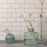 Wall of warm white medium brick metro tiles with beige grout against a grey wood worktop with two vases on top