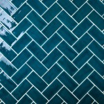 Wall of teal medium brick metro tiles with white grout laid in a herringbone tile pattern