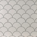 Wall of warm white scallop tiles with medium grey grout laid in a fish scale pattern ideal for kitchens and bathrooms