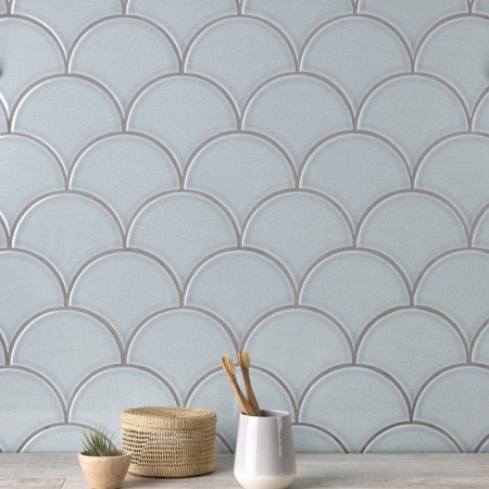 Wall of pale silver blue scallop tiles with medium grey grout against an oak worktop behind some home accessories