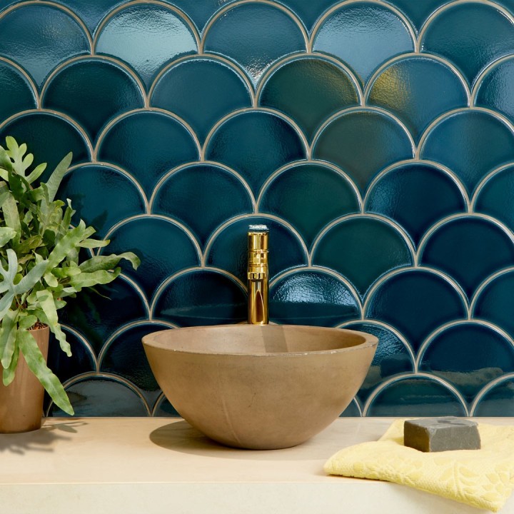 Dark blue scallop tiles with limestone grout behind a sandstone basin and gold tap next to a house plant and soap bar