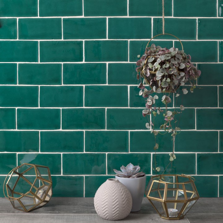 Wall of bottle green medium brick metro tiles with jasmine grout against an oak worktop with home accessories on top