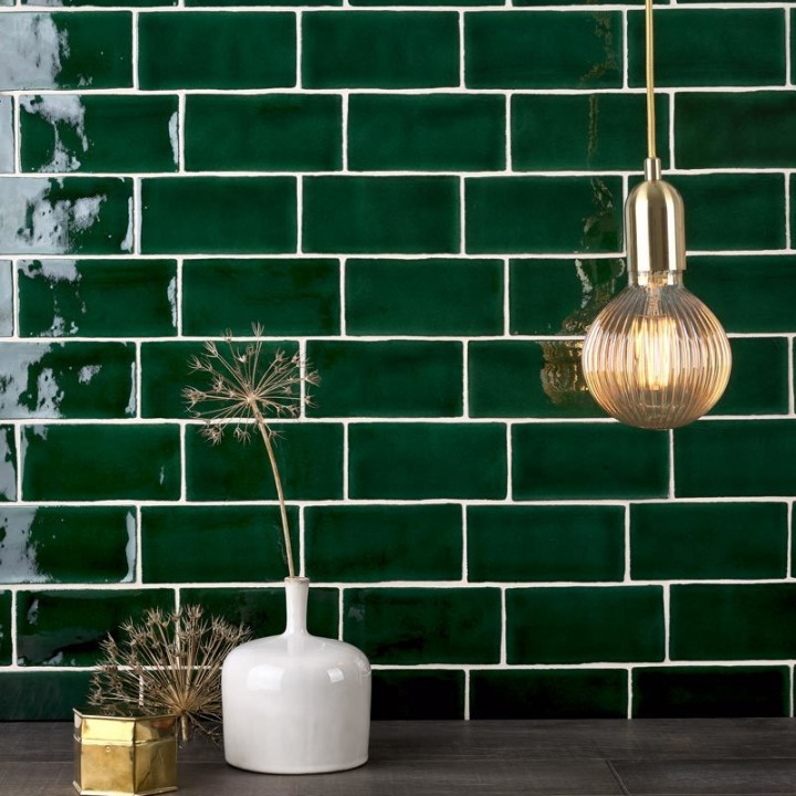 Wall of emerald green medium brick metro tiles with white grout against a grey oak worktop with home accessories on top