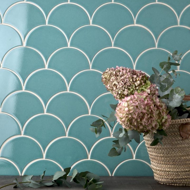 Wall of aqua green scallop tiles with jasmine grout against an oak work top behind a vase of hydrangea