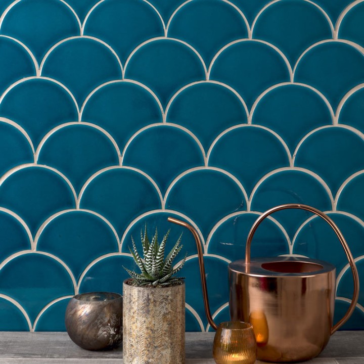 Wall of teal scallop tiles with white grout against an worktop behind some home accessories
