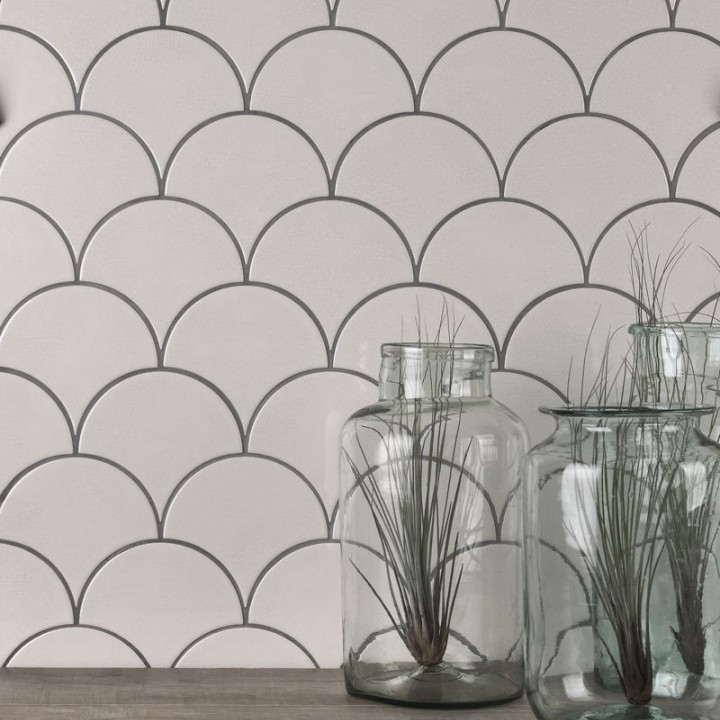 Wall of warm white scallop tiles with medium grey grout against an oak work top behind some vases