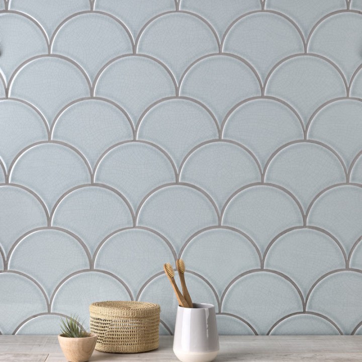 Wall of pale silver blue scallop tiles with medium grey grout against an oak worktop behind some home accessories