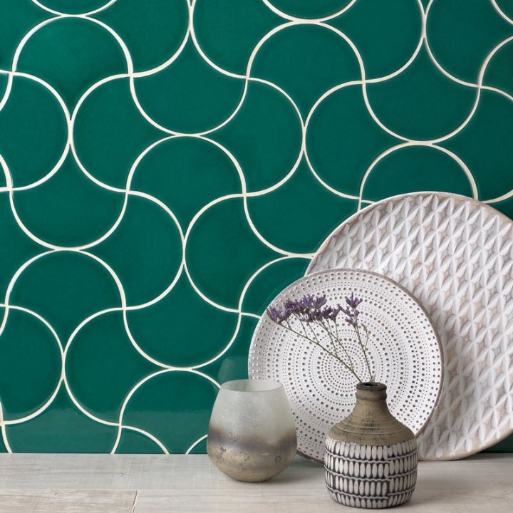 Wall of bottle green scallop tiles with jasmine grout against an oak worktop behind some ornamental plates