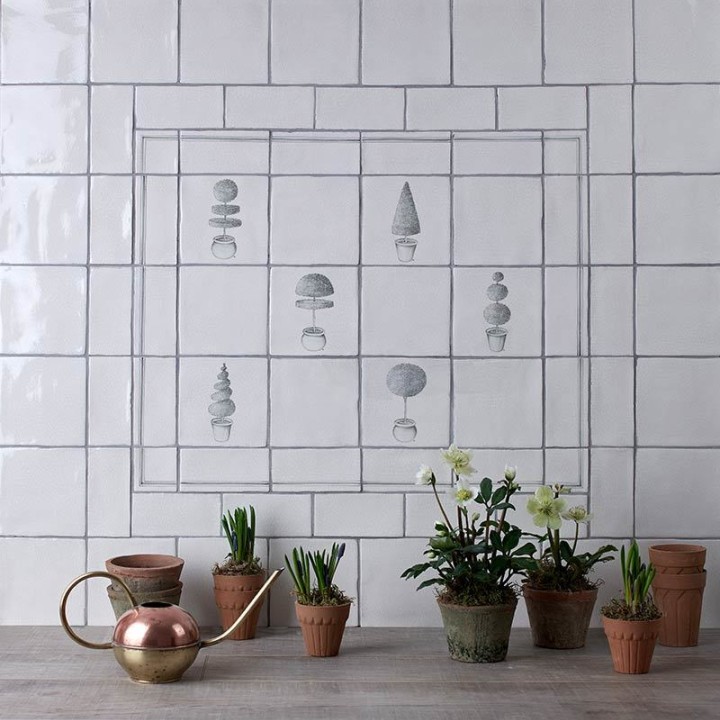 Wall of antique white square tiles with topiary illustrations in a charcoal style framed with charcoal lines