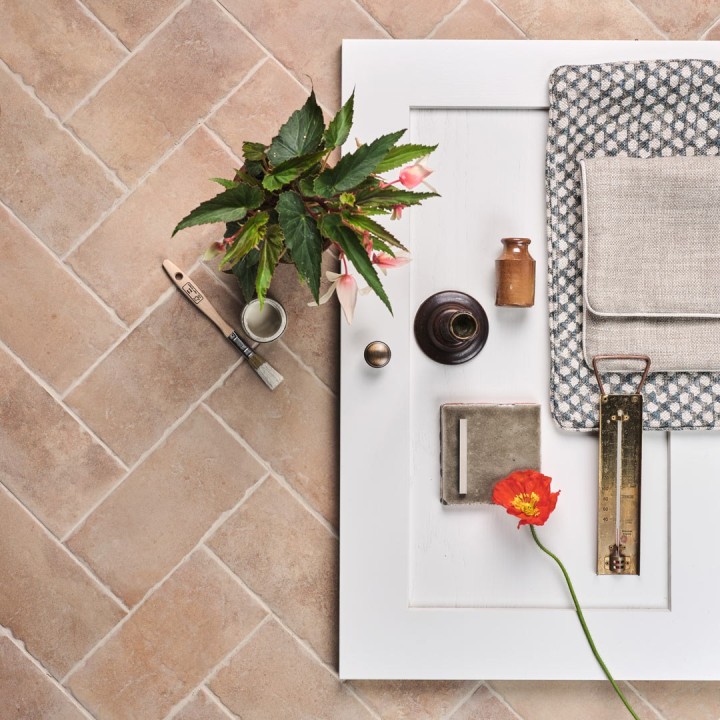 Flatlay of pale terracotta Seville Small Brick tiles laid in a herringbone pattern and finished with Limestone grout with Fermoie fabric swatches and a green tile