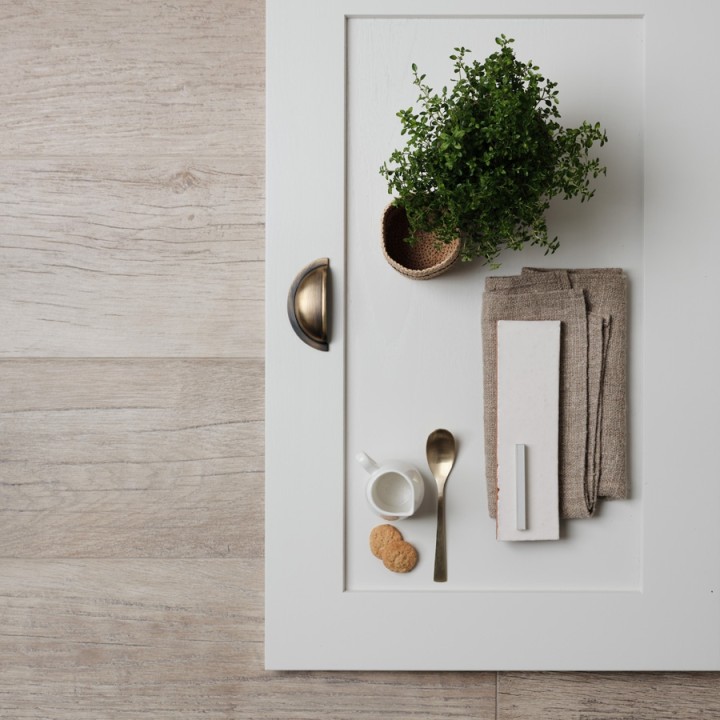 Flatlay of weathered oak wood effect floor tiles beneath a white kitchen cabinet door and a skinny brick tile