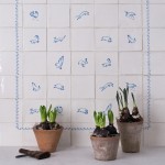 Panel of delft tiles with animal illustrations framed with a blue border. Three pots of spring bulbs are in front