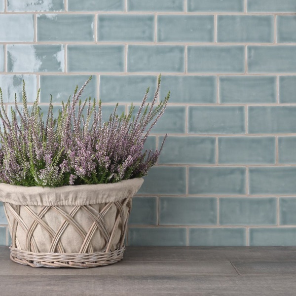 A sideboard with planter and heather against a wall of turquoise medium brick tiles