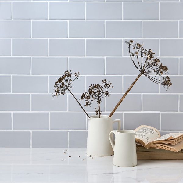 A vase of dried flowers in front of a wall of medium brick pale blue matt tiles