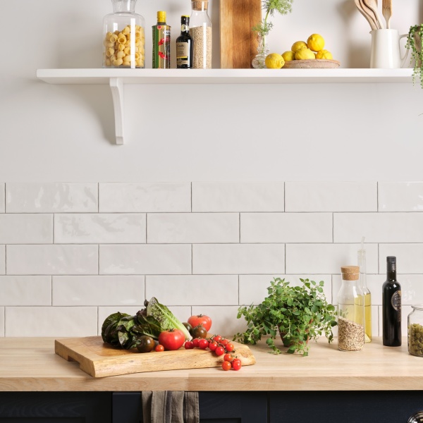 A dark blue kitchen with salad items on the counter and long brick white tiled backsplash