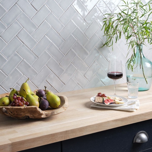 Pine sideboard with fruit bowl and wine glass in a dark blue kitchen, with silver-blue small brick tiles