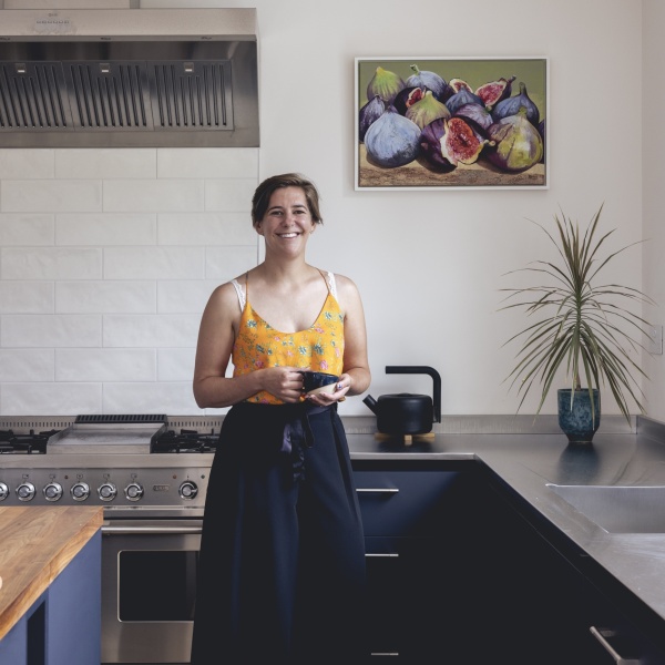 Woman standing in a beautiful dark blue kitchen with long brick white tiles above a range cooker