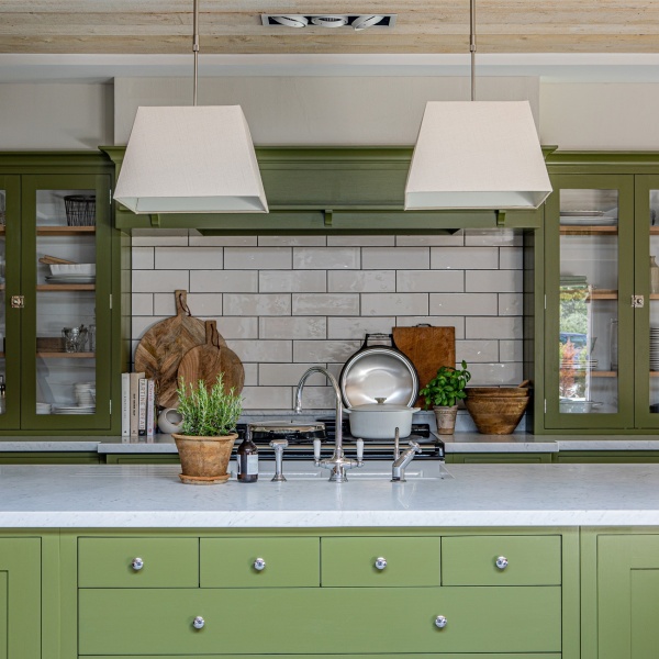 A green kitchen with white long brick tiles above a range cooker