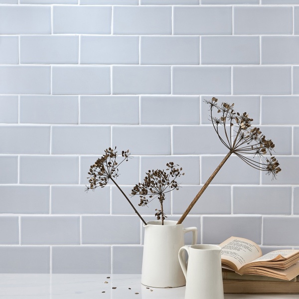 Wall of skinny pale blue matt metro tiles with silver grey grout laid in a herringbone tile pattern styled with a pile of plates